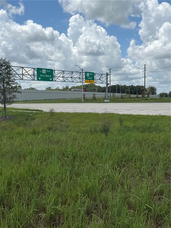 A highway overpass features green road signs for Vero Beach and Tampa under a cloudy sky — MIAMI STREET, LAKE WALES, FL