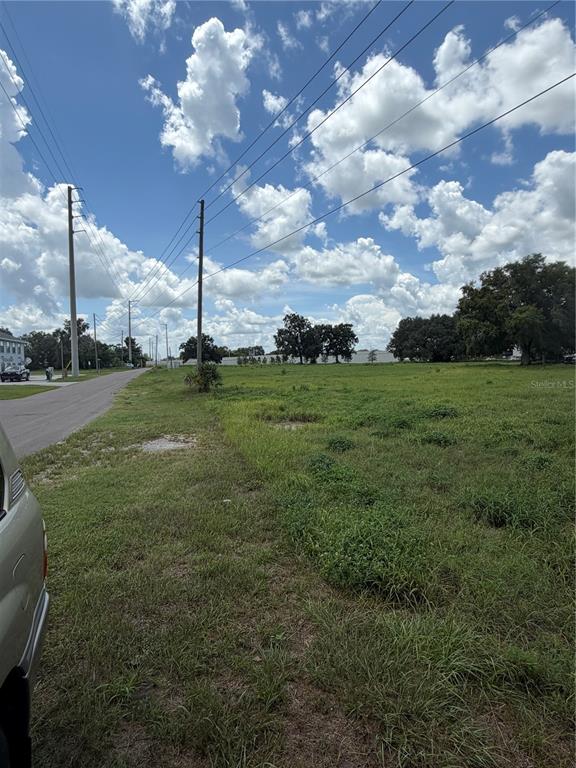 A grassy, undeveloped lot sits next to a paved road under a cloudy blue sky — MIAMI STREET, LAKE WALES, FL