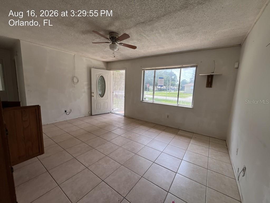 An empty living room with light-colored floor tiles, a ceiling fan, and a front door — 4409 WATCH HILL ROAD, ORLANDO, FL
