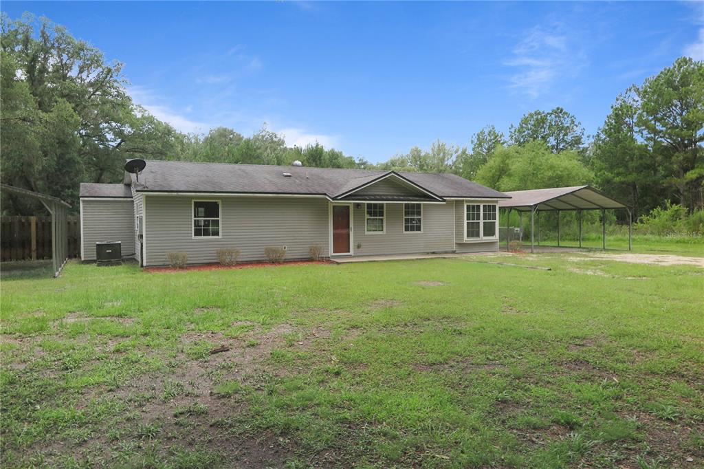 A single-story house with gray siding, a metal carport, and a large grassy yard — 11320 122ND TRAIL, LIVE OAK, FL