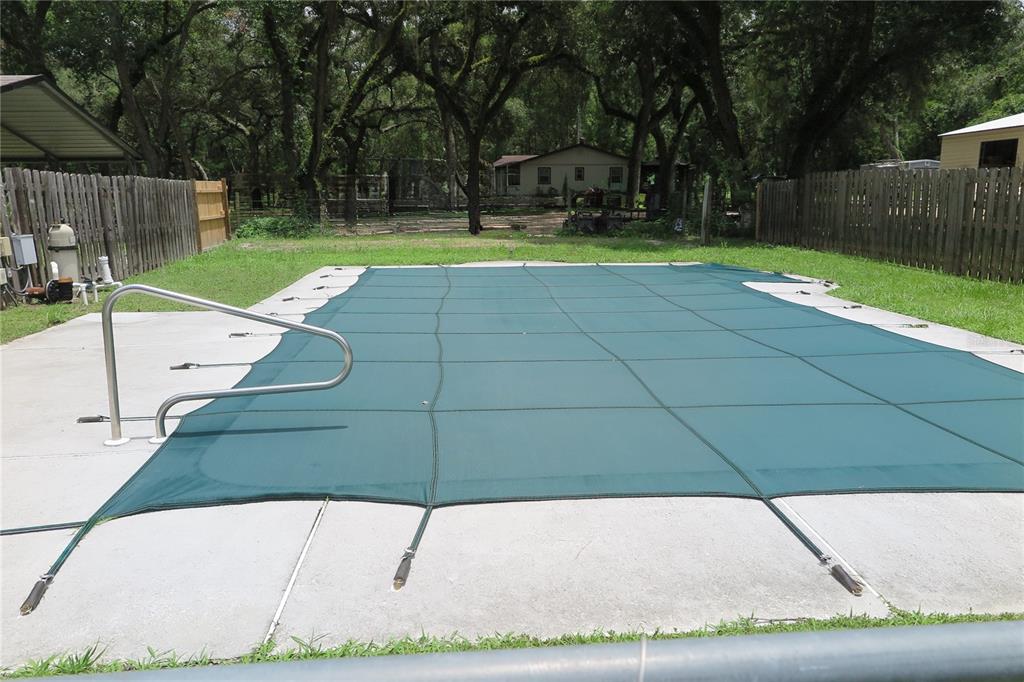 A rectangular swimming pool is covered with a green mesh safety cover in a backyard — 11320 122ND TRAIL, LIVE OAK, FL