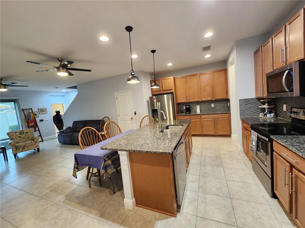 A kitchen with wood cabinets, granite countertops, and an island opens into a living area — 5514 VIOLA LEE WAY, LUTZ, FL