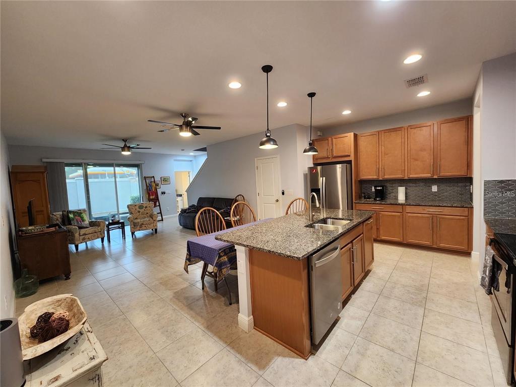 An open-concept kitchen and living area features tile flooring, wood cabinets, and a granite island — 5514 VIOLA LEE WAY, LUTZ, FL