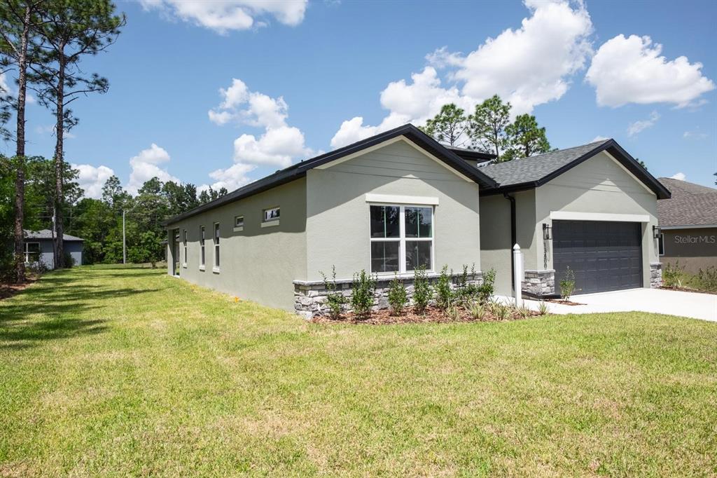 A single-story house with light green stucco, stone accents, and a dark garage door — 2420 SW 159 LANE, OCALA, FL
