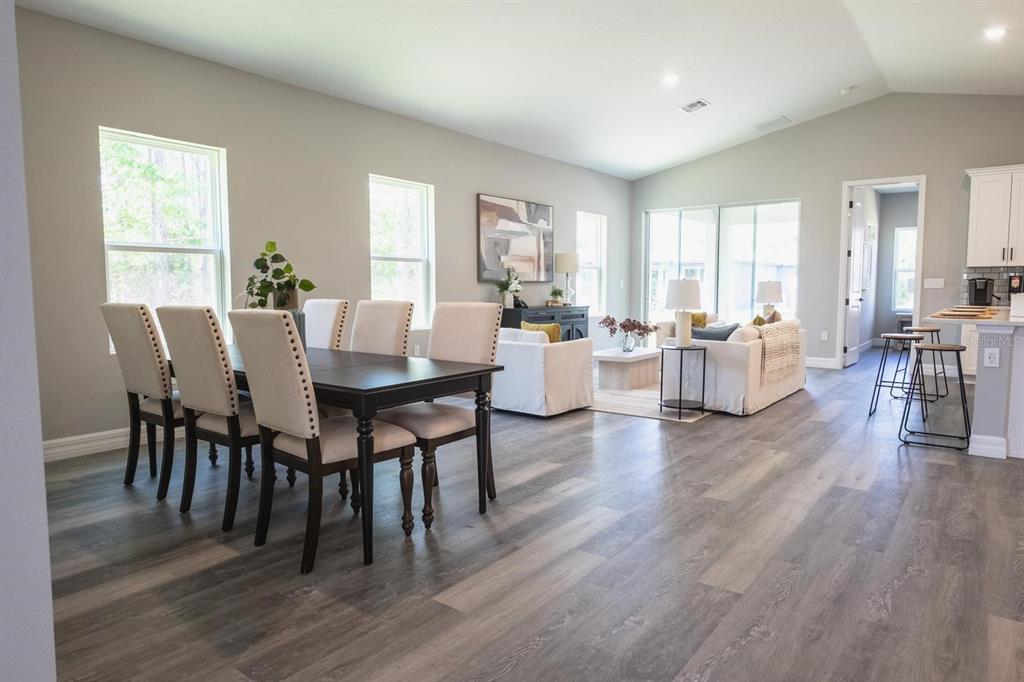 An open-concept living and dining area features wood-look flooring, neutral walls, and large windows — 2420 SW 159 LANE, OCALA, FL