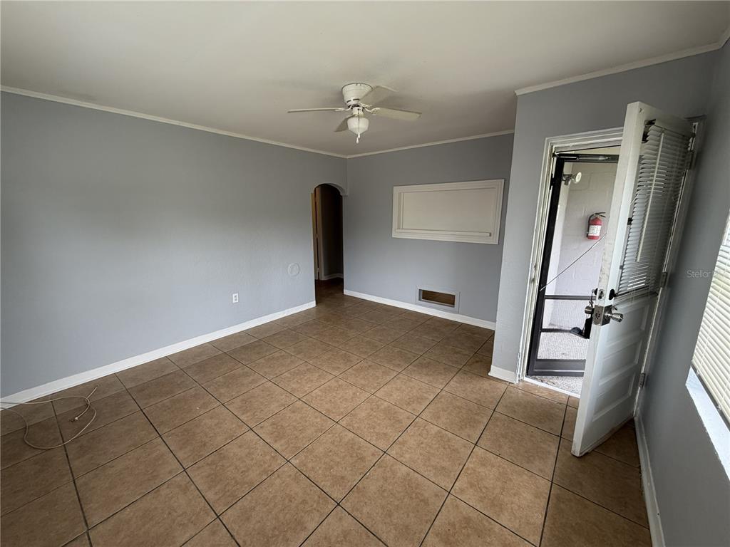 An empty room features light gray walls, brown tile flooring, a ceiling fan, and an entryway — 370 3RD STREET NW, LARGO, FL
