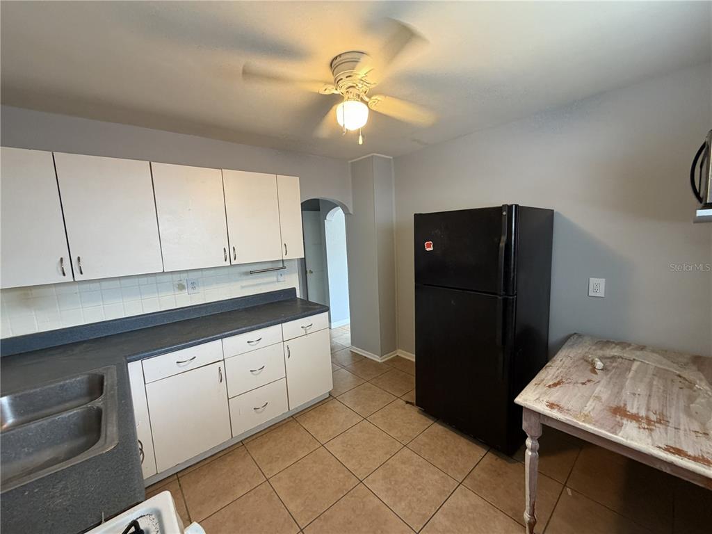 A kitchen with white cabinets, a black refrigerator, dark countertops, and tile flooring — 370 3RD STREET NW, LARGO, FL