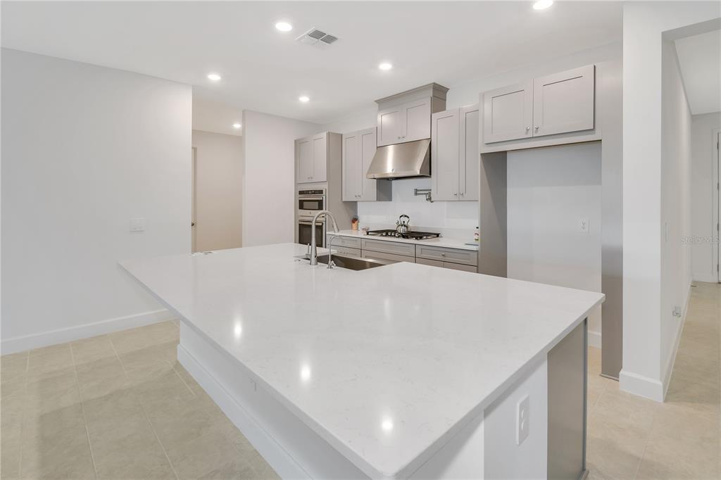 A modern kitchen features a large white quartz island, gray cabinetry, and stainless steel appliances — 1224 WATERVIEW RIDGE CIRCLE, APOPKA, FL