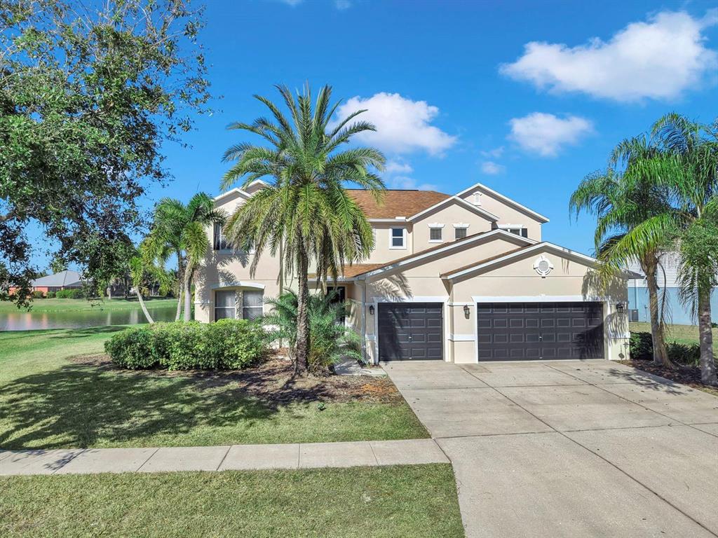 A two-story suburban house with a three-car garage, palm trees, and a pond view — 5457 SANDY SHELL DRIVE, APOLLO BEACH, FL