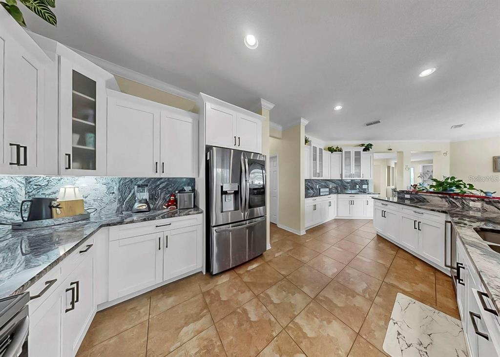 A kitchen features white cabinets, dark marble countertops, stainless steel appliances, and tan tile flooring — 5457 SANDY SHELL DRIVE, APOLLO BEACH, FL