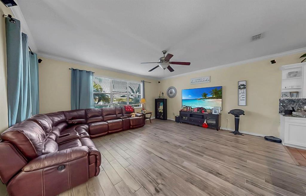 A spacious living room features a large brown sectional sofa, wood-look flooring, and a television — 5457 SANDY SHELL DRIVE, APOLLO BEACH, FL