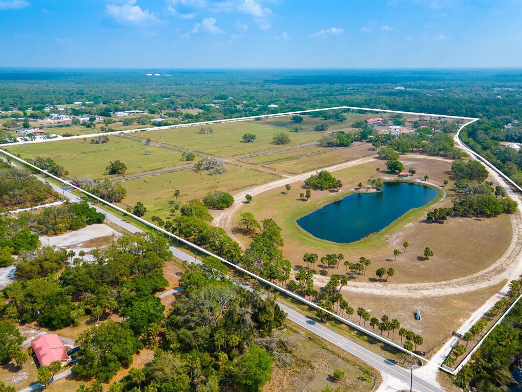An aerial view shows a large, fenced rural property featuring a pond and pasture land — 600 N JACKSON ROAD, VENICE, FL