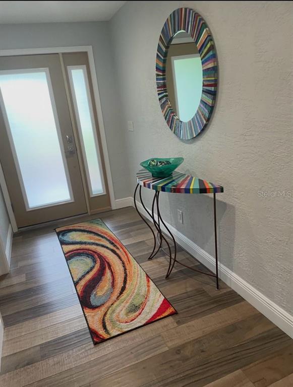 An entryway features wood-look flooring, a colorful semi-circular console table, and a matching round mirror — 19 SANCHEZ AVENUE, ORMOND BEACH, FL