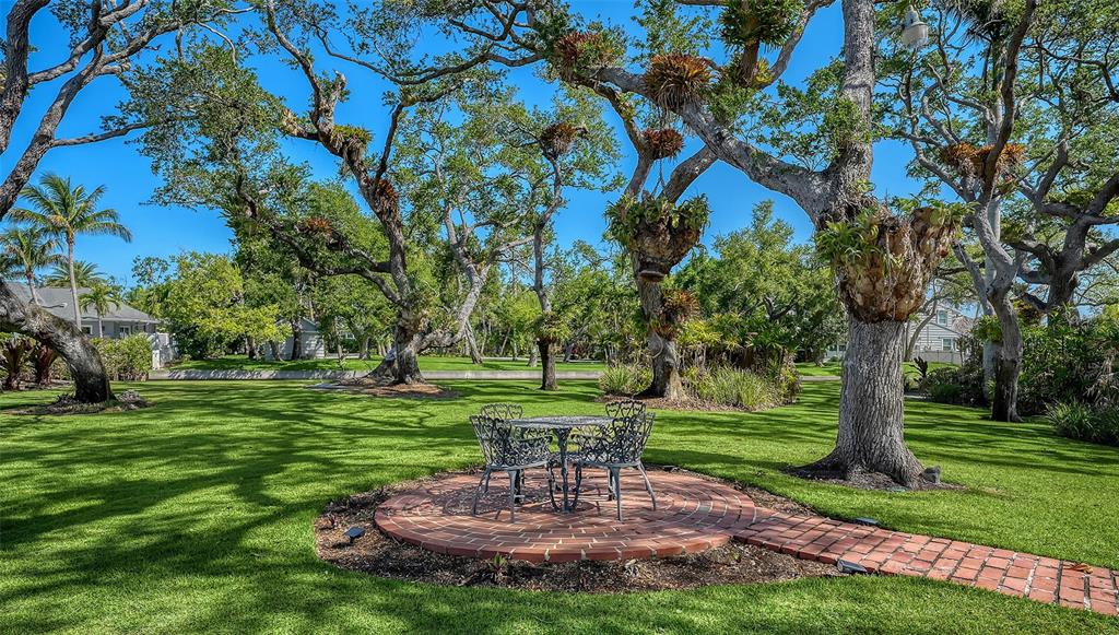 A circular brick patio with a metal table and chairs sits on a grassy lawn — 1249 S BASIN LANE, SARASOTA, FL