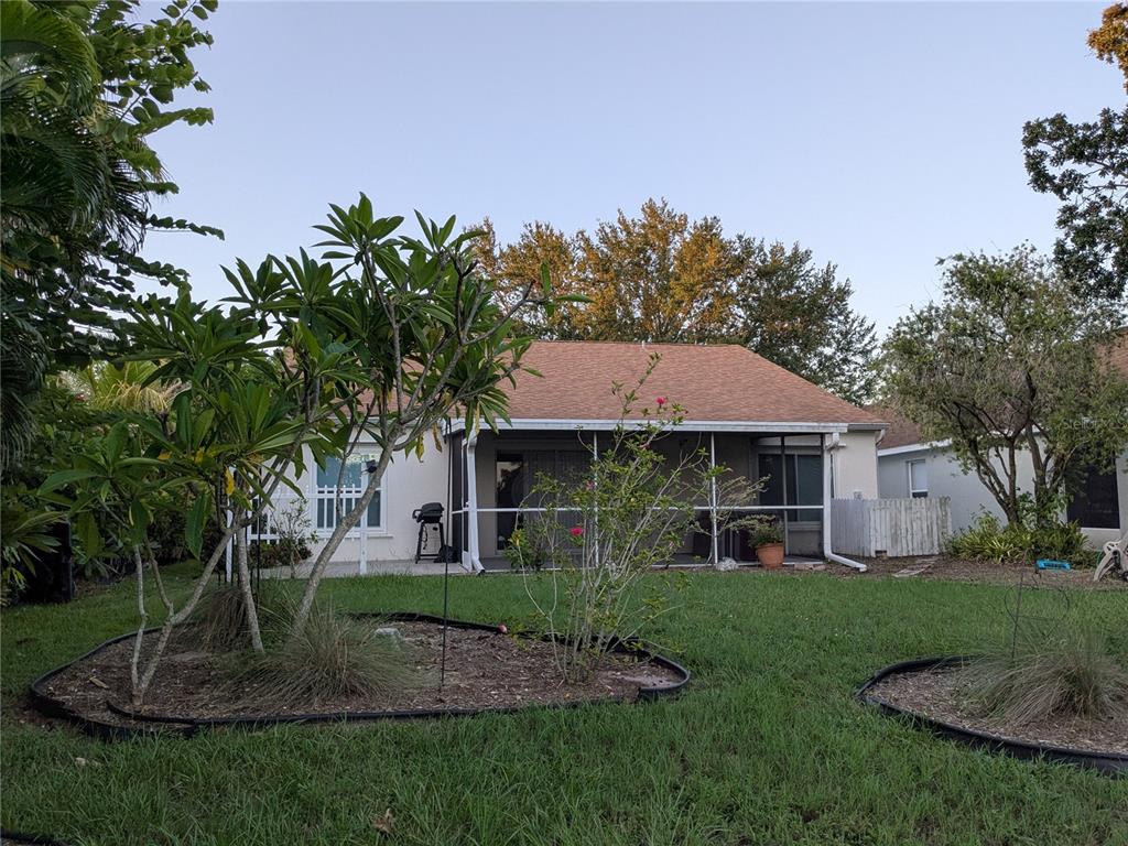 A backyard view of a house with a screened-in patio and landscaped garden beds — 10507 WALKER VISTA DRIVE, RIVERVIEW, FL