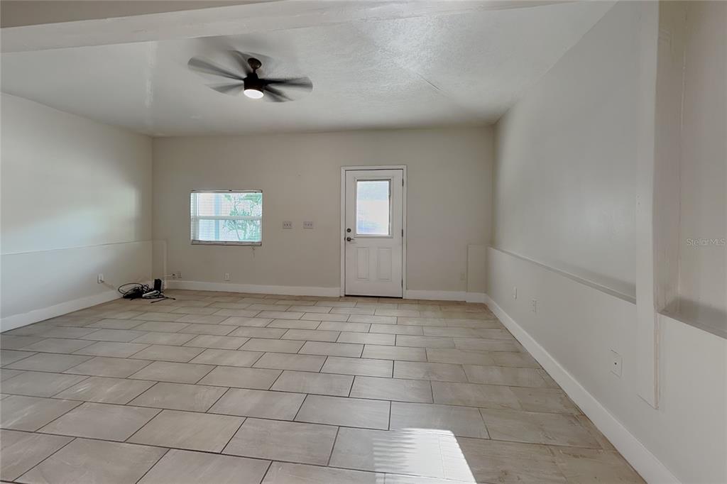 An empty room features light-colored tile flooring, a ceiling fan, and a white exterior door — 3801 1/2 W PALMIRA AVENUE, TAMPA, FL