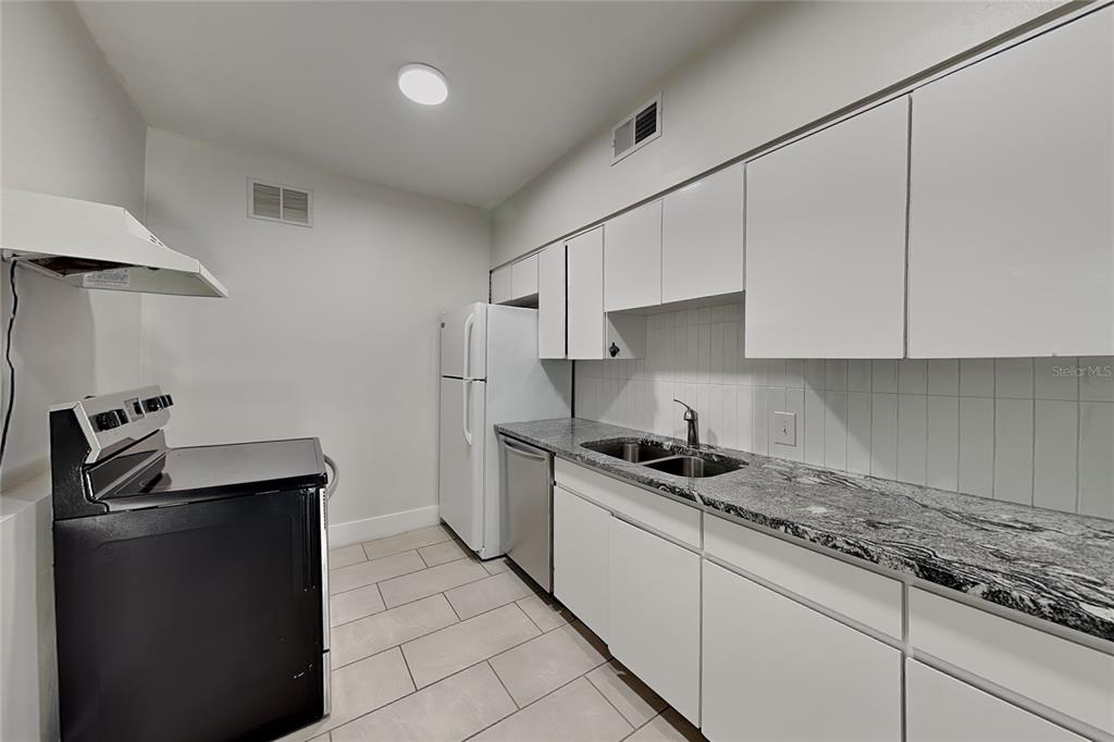 A galley kitchen features white cabinets, granite countertops, a black stove, and light tile flooring — 3801 1/2 W PALMIRA AVENUE, TAMPA, FL