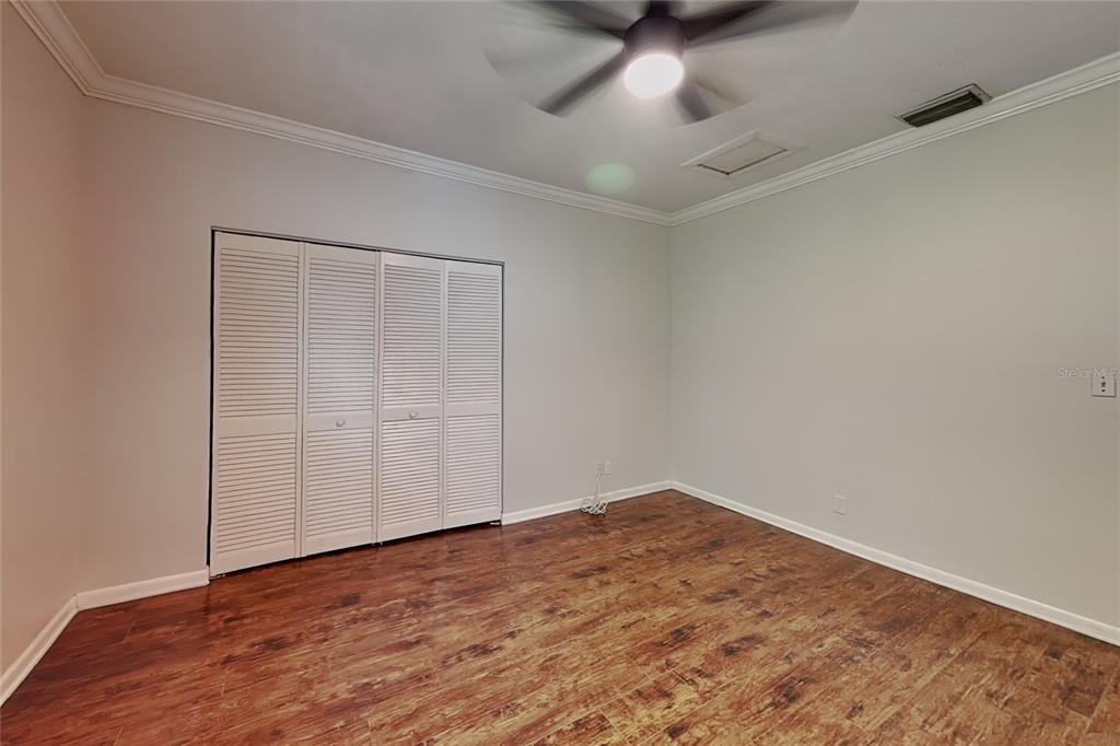 An empty bedroom features light gray walls, wood-look flooring, a ceiling fan, and louvered closet doors — 3801 1/2 W PALMIRA AVENUE, TAMPA, FL