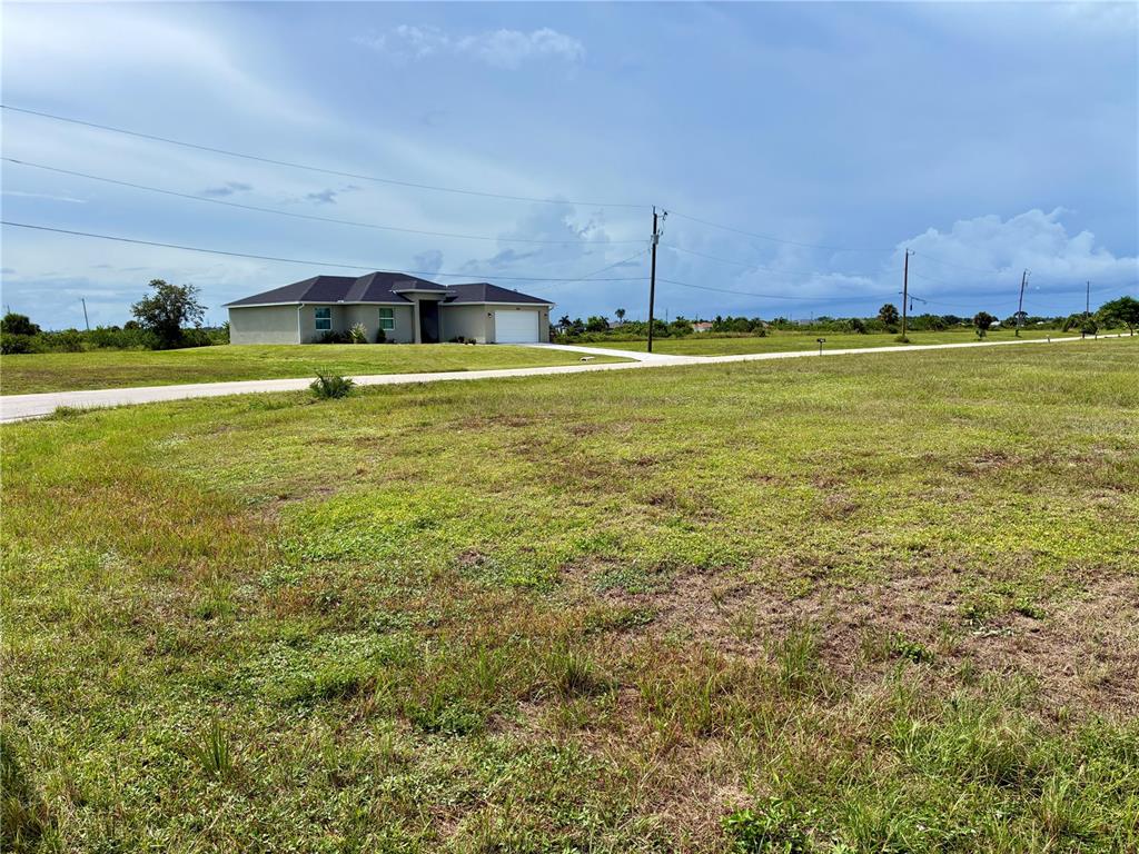 A single-story house sits on a large, grassy, undeveloped lot under a cloudy sky — 3623 NW 38TH LANE, CAPE CORAL, FL