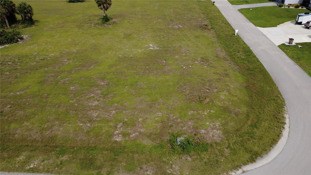 An aerial view shows a vacant, grassy corner lot bordered by a paved road — 3623 NW 38TH LANE, CAPE CORAL, FL