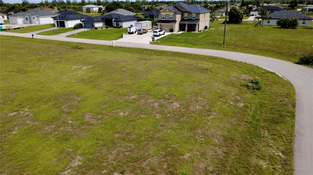 An aerial view shows a large, vacant grassy lot next to a paved road and houses — 3623 NW 38TH LANE, CAPE CORAL, FL