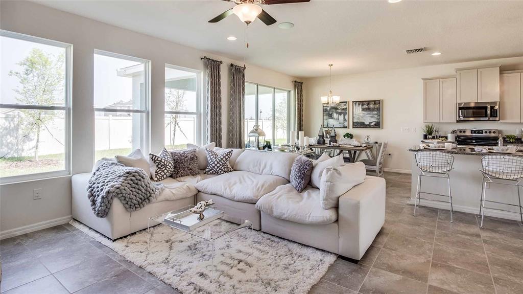 A bright open-concept living room and kitchen featuring a large sectional sofa and tile flooring — 17119 JAMES TRAIL, PARRISH, FL