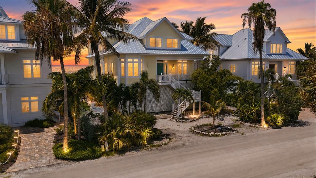 An exterior view of three elevated coastal homes with metal roofs and palm trees at sunset — 7394 PALM ISLAND DRIVE, PLACIDA, FL