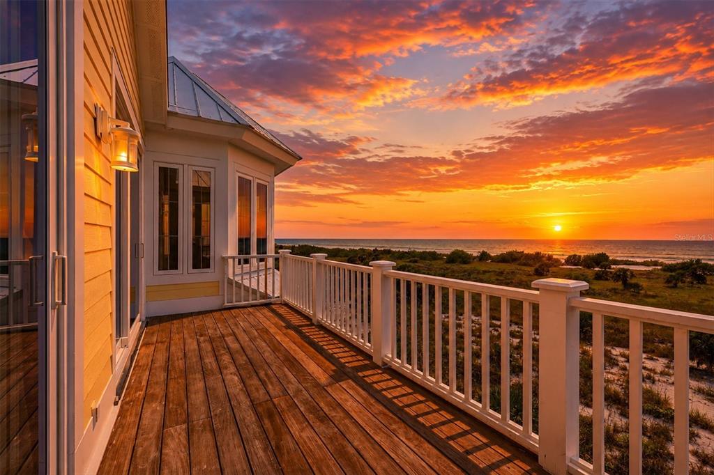 A wooden deck with a white railing overlooks a beach at sunset — 7394 PALM ISLAND DRIVE, PLACIDA, FL