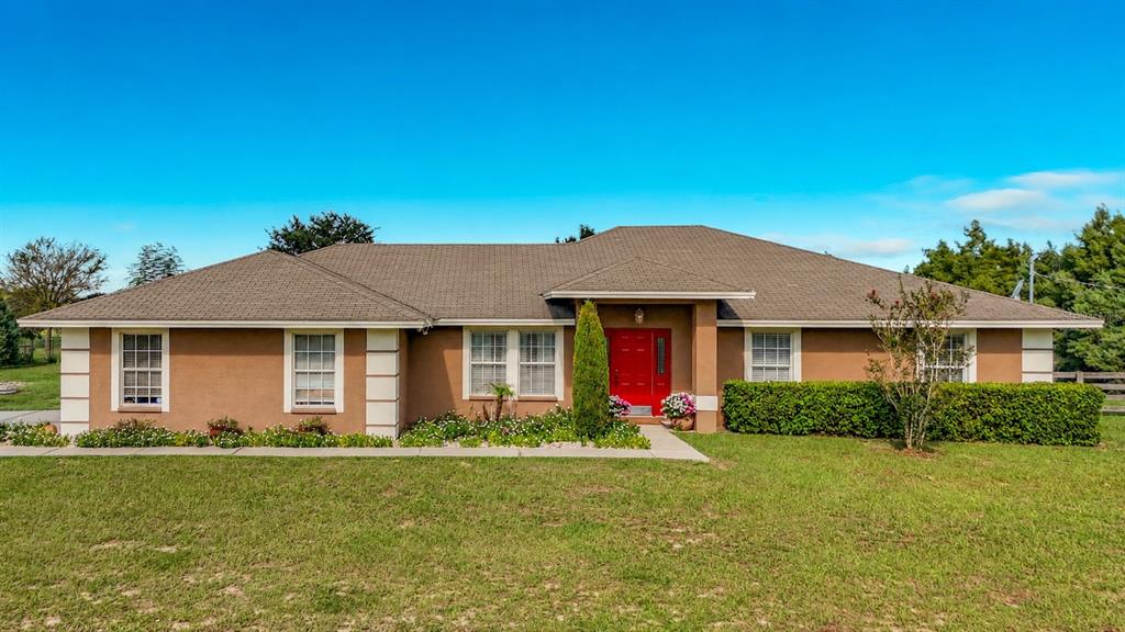A single-story house with a brown exterior, a red front door, and a grassy lawn — 18030 BAYAMON AVENUE, POLK CITY, FL