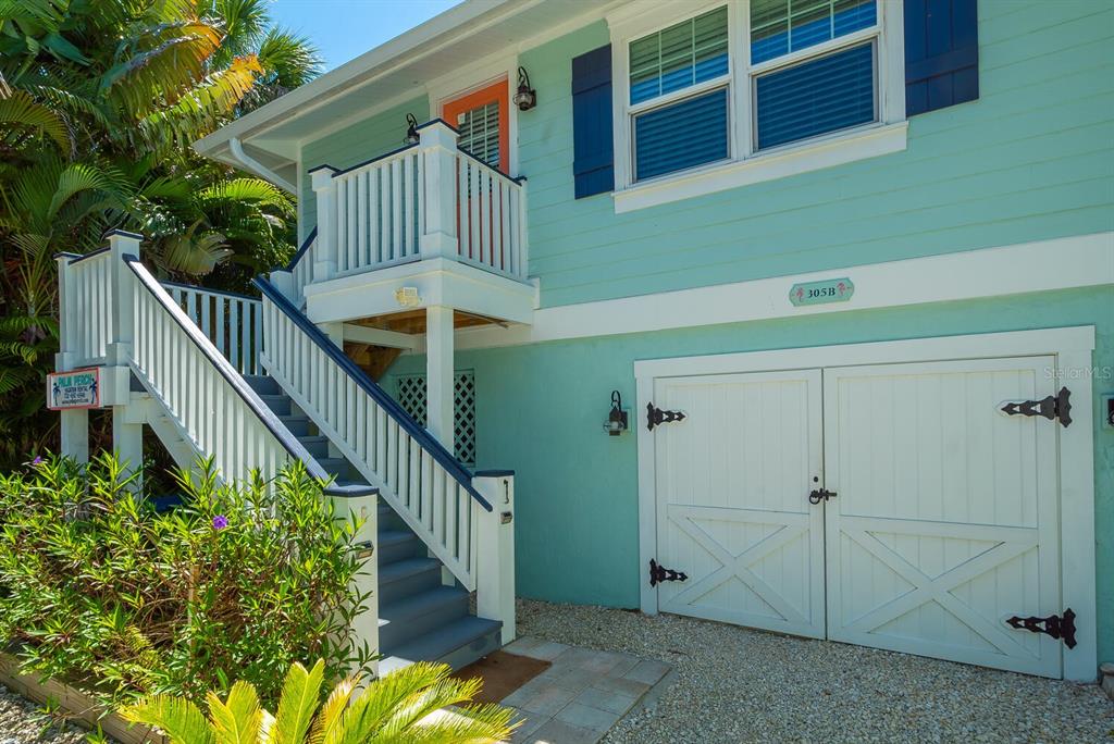 An exterior view of a teal elevated house with a white staircase and garage doors — 305 57TH STREET UNIT B, HOLMES BEACH, FL
