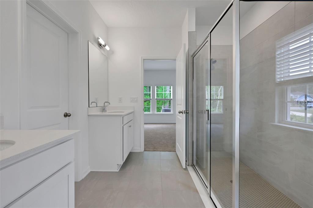 A bathroom features a glass-enclosed shower, a white vanity with a mirror, and tiled flooring — 775 FARMFIELD DRIVE, ST AUGUSTINE, FL