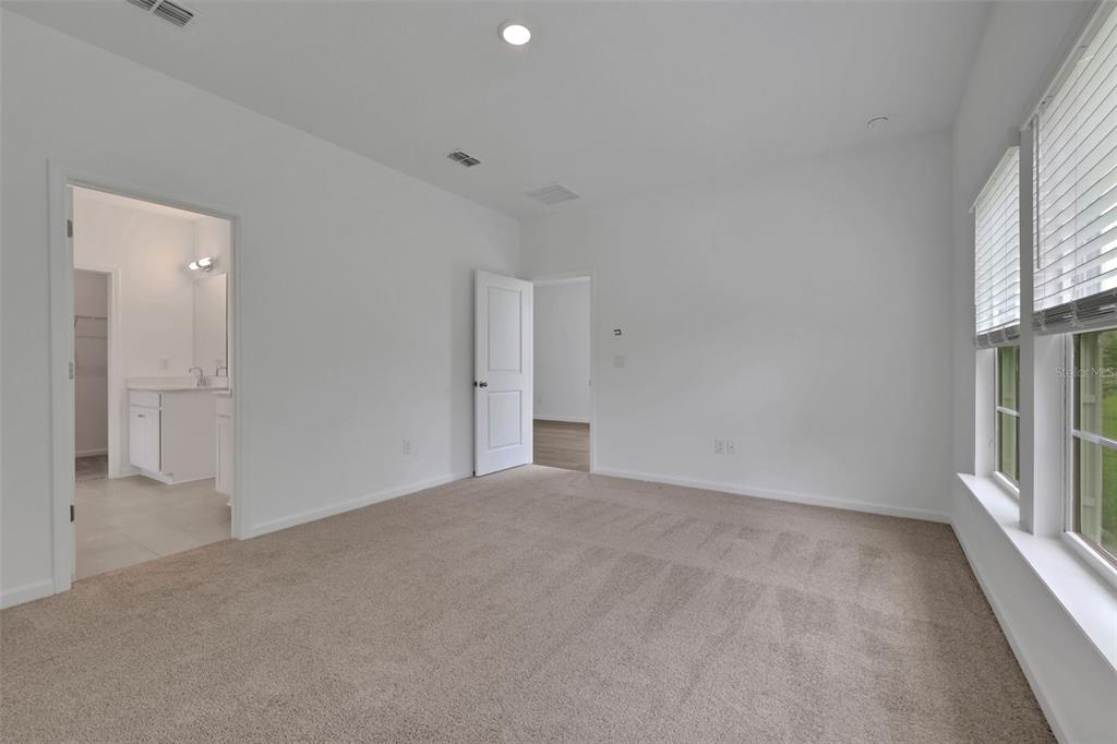 A carpeted bedroom with white walls, a doorway to a bathroom, and large windows — 775 FARMFIELD DRIVE, ST AUGUSTINE, FL