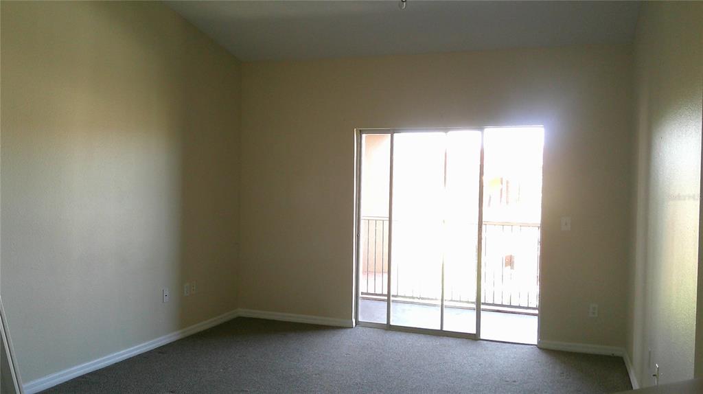 An empty bedroom features beige walls, carpeted flooring, and a sliding glass door to a balcony — 5518 METROWEST BOULEVARD UNIT 207, ORLANDO, FL