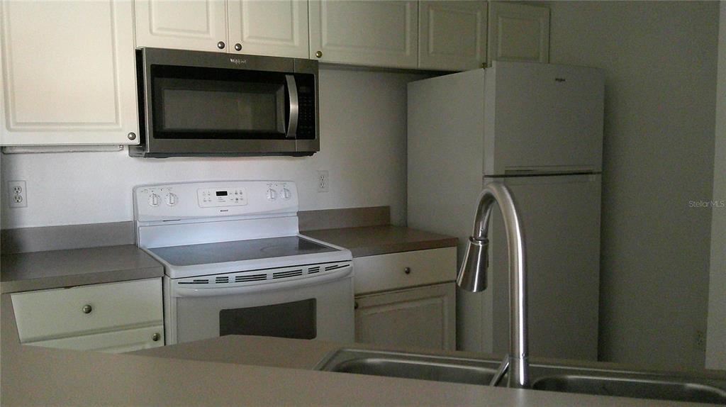A kitchen features white cabinets, stainless steel appliances, and a double-basin sink — 5518 METROWEST BOULEVARD UNIT 207, ORLANDO, FL