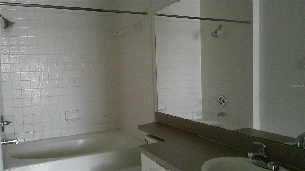 A bathroom features a white tiled shower-tub combination and a vanity with a large mirror — 5518 METROWEST BOULEVARD UNIT 207, ORLANDO, FL