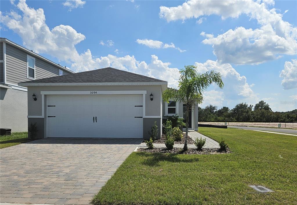 A single-story house with a two-car garage, paver driveway, and a small palm tree — 3094 SANCTUARY DRIVE, CLERMONT, FL