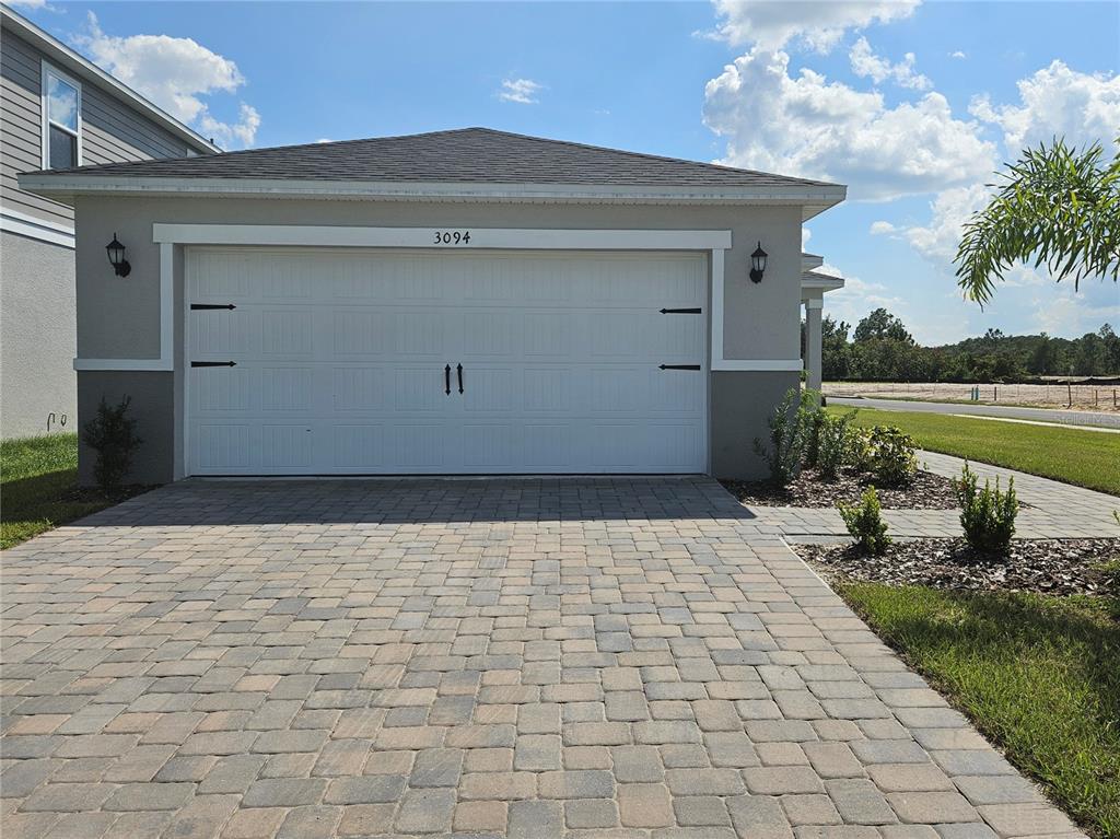 A paved driveway leads to a two-car garage with a white door and exterior lighting — 3094 SANCTUARY DRIVE, CLERMONT, FL