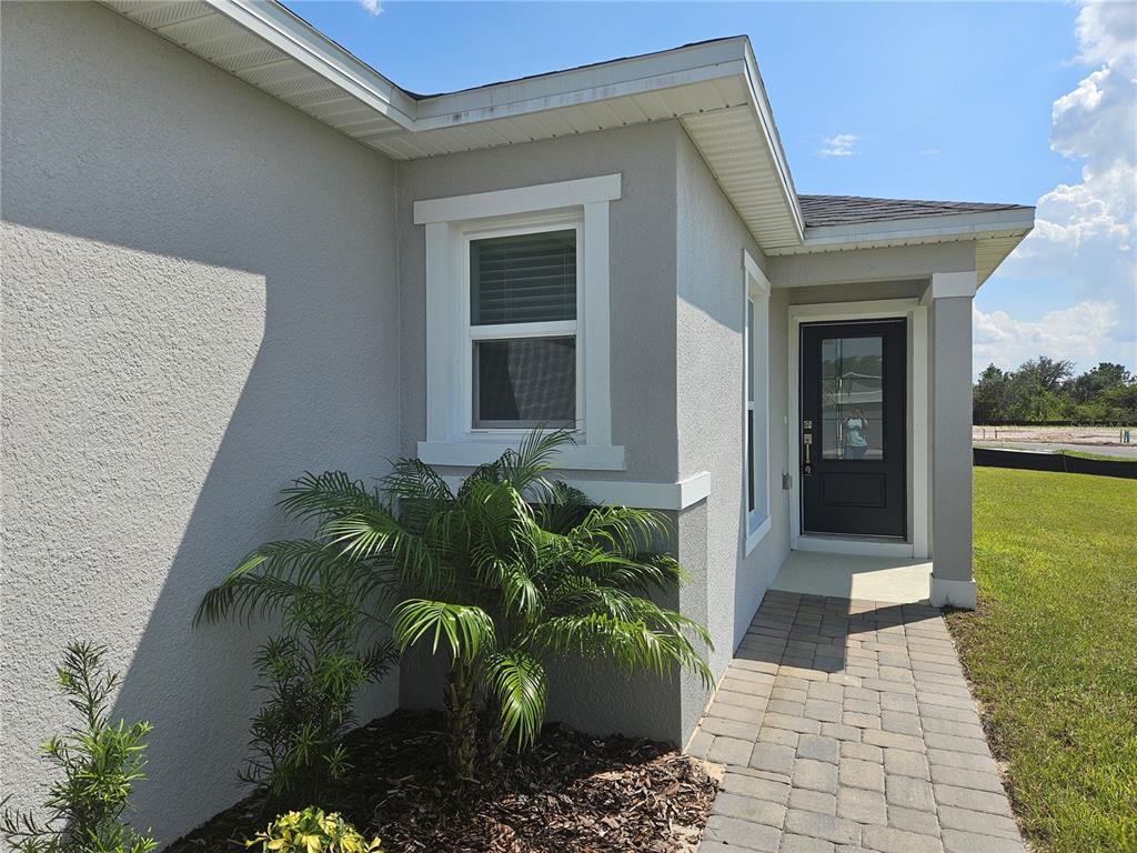 A gray stucco house exterior features a front door, a window, and a paver walkway — 3094 SANCTUARY DRIVE, CLERMONT, FL