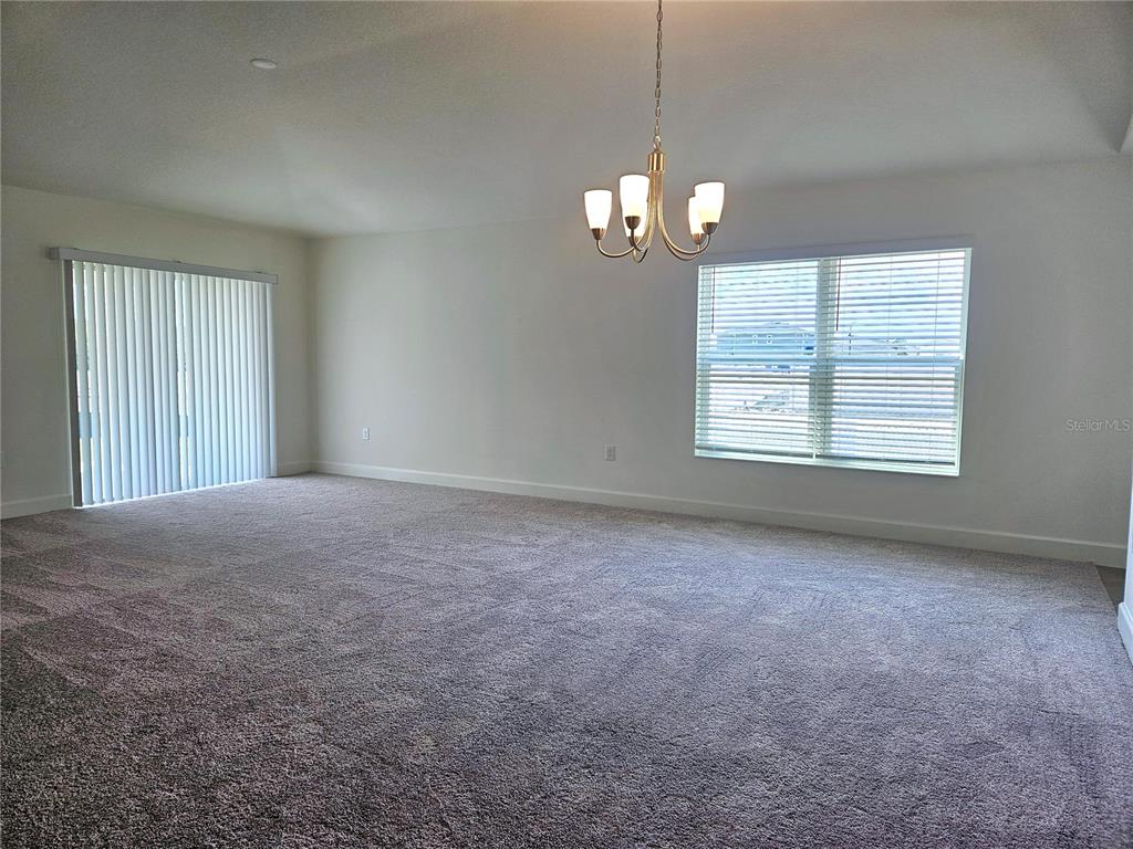 An empty room with gray carpet, a chandelier, a sliding glass door, and a window — 3094 SANCTUARY DRIVE, CLERMONT, FL
