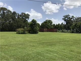 A large, grassy field features scattered trees and two shipping containers in the background — NE 36TH ST., OXFORD, FL