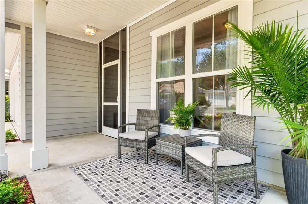 A covered front porch features gray wicker chairs, a small table, and a patterned rug — 1659 NW 34TH AVENUE, GAINESVILLE, FL