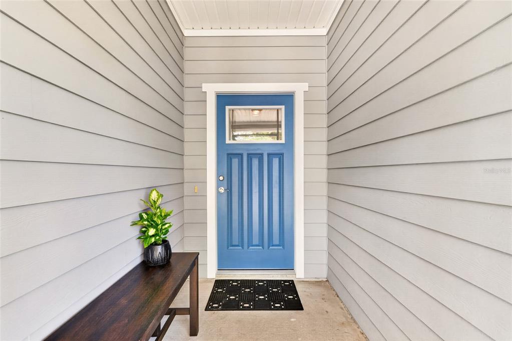 A blue front door is centered between gray horizontal siding walls on a covered porch — 1659 NW 34TH AVENUE, GAINESVILLE, FL