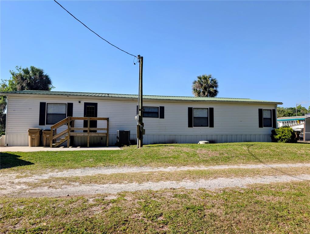 A single-story mobile home with a green metal roof and a wooden entrance deck — 25836 MANHATTAN LANE, ASTOR, FL