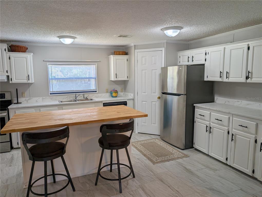 A kitchen features white cabinets, stainless steel appliances, a wooden island, and light tile flooring — 25836 MANHATTAN LANE, ASTOR, FL