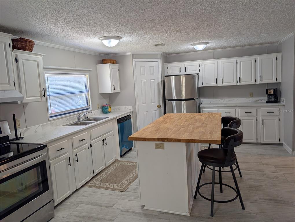 A kitchen features white cabinets, stainless steel appliances, a wooden island, and light-colored flooring — 25836 MANHATTAN LANE, ASTOR, FL