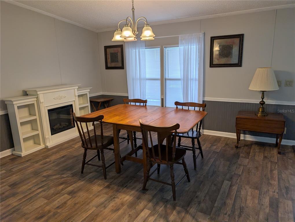 A dining room features wood-look flooring, a fireplace, a wooden table, and a chandelier — 25836 MANHATTAN LANE, ASTOR, FL