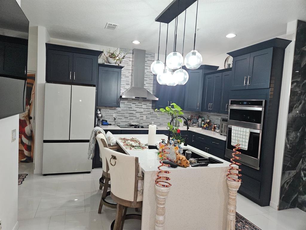 A modern kitchen features dark blue cabinets, a white quartz island, and glass pendant lights — 3565 CLAY BRICK ROAD, HARMONY, FL