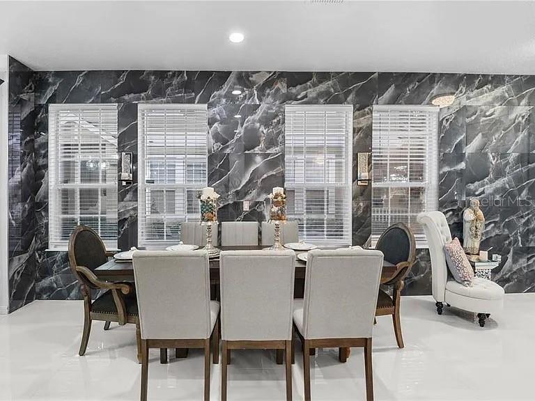 A dining room features a dark marble accent wall, white tile floors, and six chairs — 3565 CLAY BRICK ROAD, HARMONY, FL