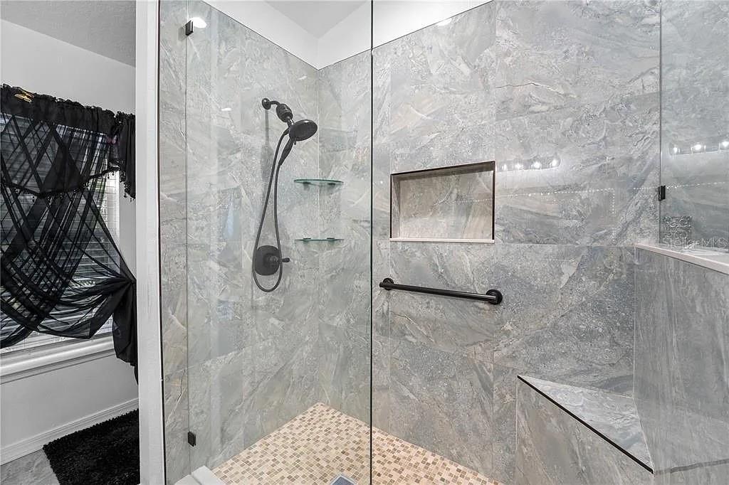 A walk-in shower features gray marble-look tile walls, a glass door, and a built-in bench — 3565 CLAY BRICK ROAD, HARMONY, FL