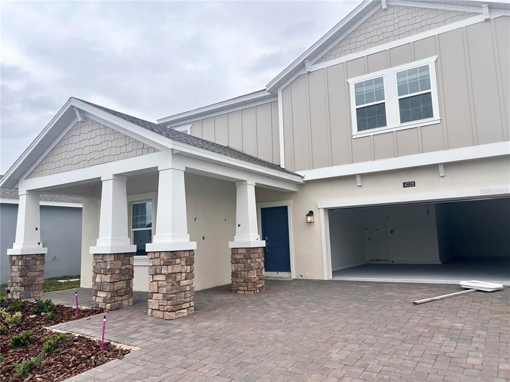 A two-story house exterior features a stone-based covered porch, a blue door, and a garage — 4028 REDBRIDGE LOOP, DAVENPORT, FL